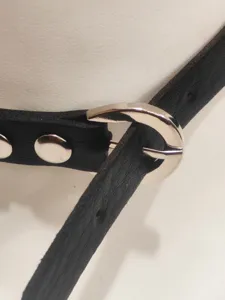 Close-up detail of black leather punk choker featuring a shiny silver metal buckle and metal rivet.
