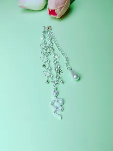 Detailed view of silver snake anklet with rhinestones and pearl pendant for summer beach style.
