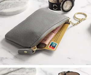 Grey leather coin purse detail, mini card holder with zipper and keychain on marble surface.
