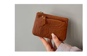 Detail view of brown leather coin purse featuring debossed floral pattern and zipper pocket.