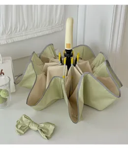 Gros plan d'un parapluie pliant chic bicolore avec protection UV et joli nœud décoratif.