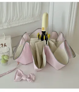 Vue détaillée du parapluie pliable rose et beige avec accessoire nœud sur une table blanche.