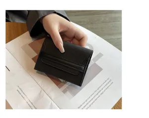 Close-up of minimalist black genuine leather card holder, compact trifold design with flap.