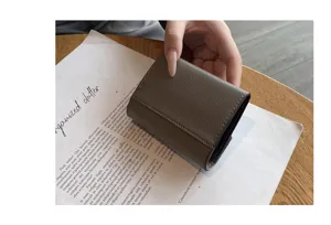 Gros plan d'un portefeuille en cuir gris minimaliste tenu en main, montrant texture et design fin.