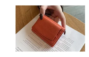 Detail shot of orange genuine leather mini trifold wallet held by hand on wooden desk background.