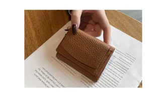 Detail shot of brown leather trifold mini wallet with grain texture and snap button.