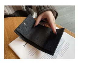 Close-up detail of black genuine leather short trifold wallet held by hand on wooden table.