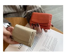 Detailed view of compact trifold leather wallets in beige and orange with pebble texture.