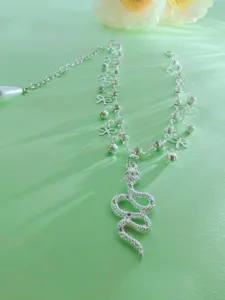 Detailed view of silver layered anklet with snake pendant, bows, and rhinestones on green.