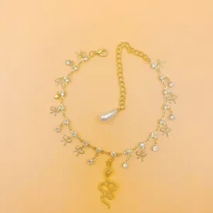 Gold rhinestone snake anklet with bow charms, elegant tassel chain and faux pearl detail for women.