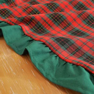 Vue détaillée de la nappe de Noël à carreaux rouge et vert avec une jolie bordure à volants.