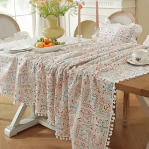 Detail view of pastoral floral tablecloth with cute pom-pom fringe in cozy dining room setup.
