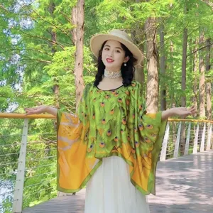 Modell trägt einen Satin-Poncho-Schal mit ethnischem Pfauenmuster im grünen Wald