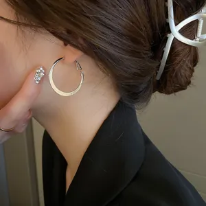 Detailed view of large silver hoop earrings worn on ear, showcasing minimalist style and shine.