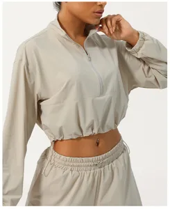 Gros plan sur la veste de sport courte beige à demi-zip, col haut et cordon de serrage.