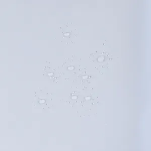 Dettaglio del tessuto impermeabile che mostra gocce d'acqua perlanti sul materiale.
