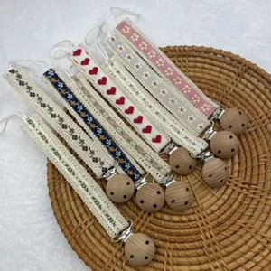 Detailansicht vintage-pastoraler bestickter Schnullerhalter mit Holzklammern und Bändern.