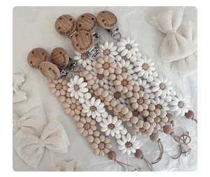 Closeup of handmade wooden pacifier clips with silicone daisy beads and natural textured flat lay.