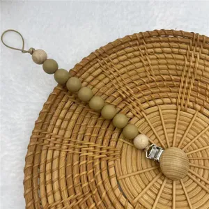 Silicone pacifier clip detail closeup showing wooden beads and metal clasp on rattan background.