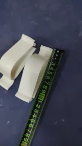 Detail shot of white plastic toilet lid fixing clips with a measuring tape for size.