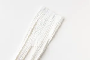 Collant neonato in maglia treccia bianca, primo piano della trama morbida fine.