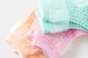 Gedetailleerde close-up van ademende mesh babysokken met kantrand in pastelkleuren, zachte stof.