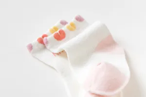 Gedetailleerde close-up van schattige katoenen baby sokken met kleurrijke harten en roze hielen.
