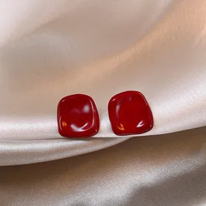 Nahaufnahme glänzender dunkelroter, unregelmäßiger Ohrringe auf Seidenstoff, elegant und chic.