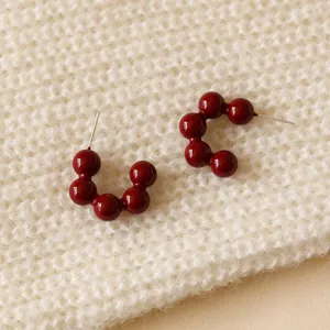 Close-up of dark red spherical beaded hoop earrings resting on a cozy knit texture.