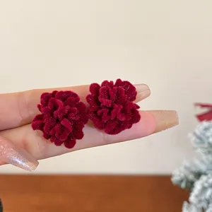 Close-up of dark red velvet flower stud earrings, showing soft texture and fine detail.