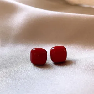 Close-up of glossy red square stud earrings on silk background, retro style autumn winter accessory.
