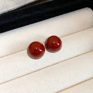 Close-up detail of dark red cabochon stud earrings placed on a beige velvet jewelry tray.
