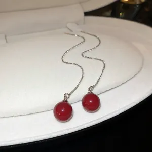 Close-up of elegant long chain drop earrings featuring smooth red sphere pendants inside a white box.