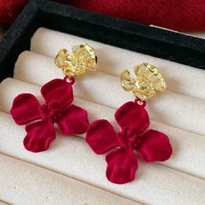Nahaufnahme eleganter roter Samt- und Goldblüten-Ohrringe mit feinen, strukturierten Details.