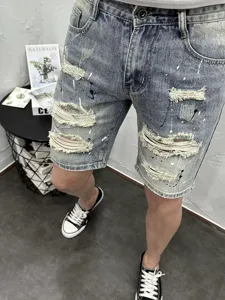 Detail view of stylish men's distressed denim shorts featuring trendy paint splatter effects.