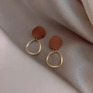 Close-up of elegant geometric pendant earrings featuring brown matte discs and irregular gold rings.