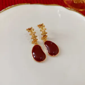 Detail view of retro gold-plated drop earrings with anchor red enamel and delicate beaded edges.