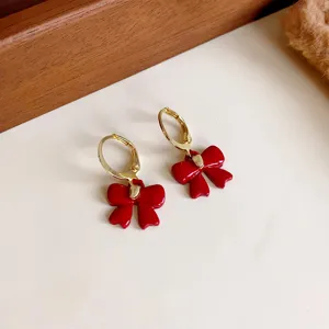 Close-up view of chic red bow earrings with gold tone hoop, delicate daily jewelry detail.