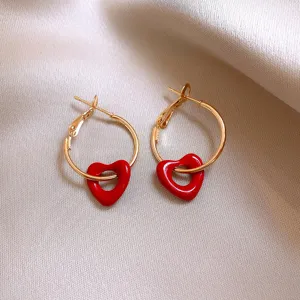 Close-up detail of retro gold-toned hoop earrings featuring vibrant red heart charms.