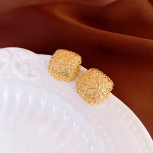 Close-up of stylish gold textured square stud earrings on a white tray, exquisite design.