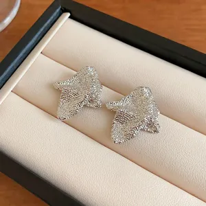 Close-up detail shot of irregular silver textured stud earrings in a luxury jewelry box display.