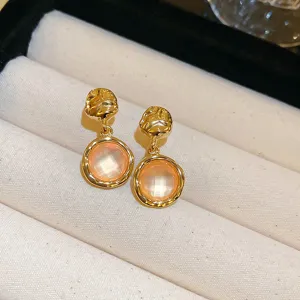 Close-up detail of chic gold-plated textured stud earrings featuring translucent peach pink stone drops.