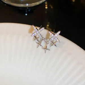 Detailed close-up view of shiny cross rhinestone stud earrings on white ceramic plate display.