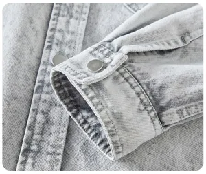 Primo piano dettaglio di polsino camicia denim grigio chiaro con bottoni metallici.
