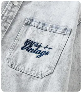 Primo piano di camicia in denim lavato vintage azzurro con taschino e ricamo.