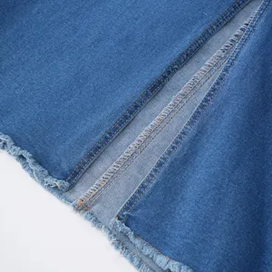 Close-up detail of blue denim midi skirt featuring raw frayed hem and front slit design.