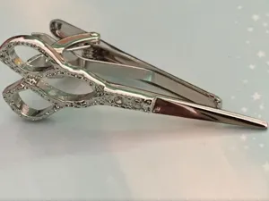 Close-up detail shot of silver metal tie clip featuring a creative scissors shape with rhinestones.