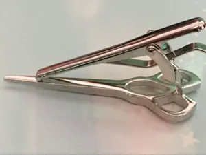 Detailed close-up view of a silver metal scissor shaped tie clip showcasing fine craft and polish.