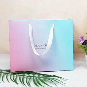 Gradient paper gift bag detail shot, elegant pink and blue design with white ribbon handles.
