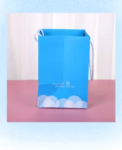 Detalle de la bolsa de regalo de papel azul con asas blancas y patrón de nubes abajo.